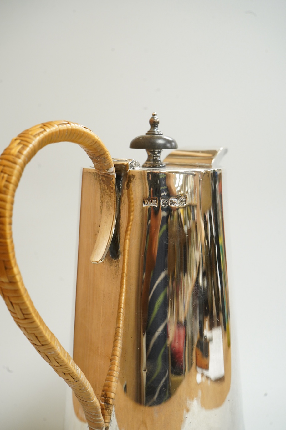 A George V silver hot water jug, by Walker & Hall, Sheffield, 1922, of tapering form, with rattan handle and circular spreading foot, height 22cm, 24.7oz.